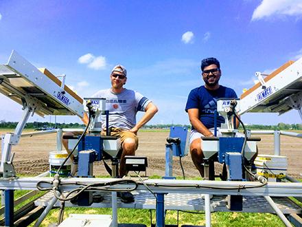 Two researchers planting corn in a field.