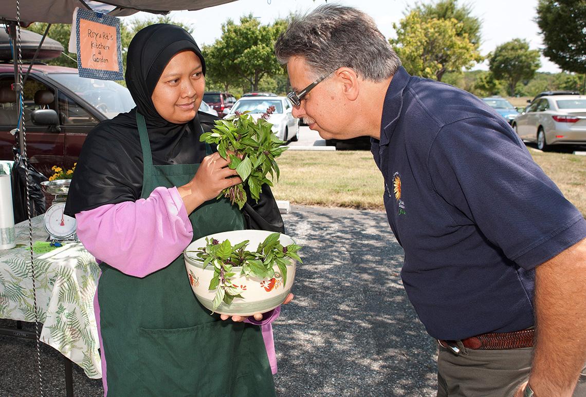 A man sniffs Thai basil held by a vendor at a farmers market