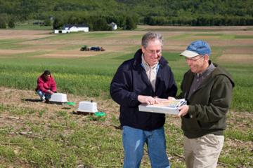 Three scientists collecting runoff samples and reviewing plot layouts in a field