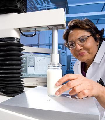 ARS food technologist Mukti Singh holding a glass jar of yogurt under a machine.
