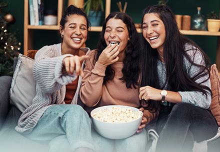Three women siting on a sofa eating from a large bowl of popcorn.