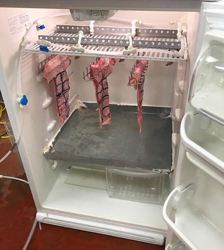 Cuts of meat hanging in a refrigerator.