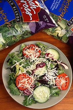 Packaged bags of salad greens next to a salad on a plate.