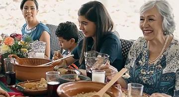 A smiling, multi-generational group of people sits at a table set with food.