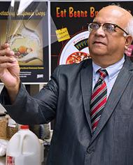 A man in a suit jacket, tie, and glasses holds up and looks at a clear rectangular sheet